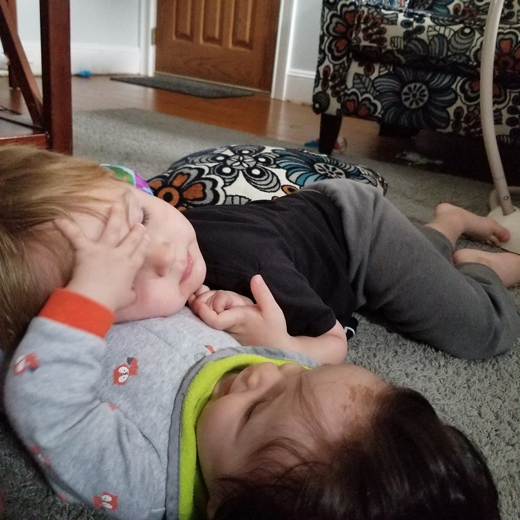 A toddler boy laying with his baby brother