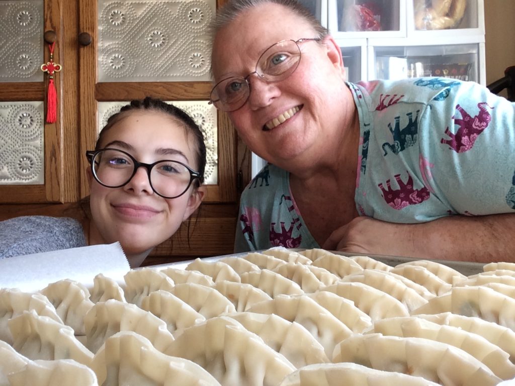 Woman poses with her granddaughter in front of a tray of homemade dumplings